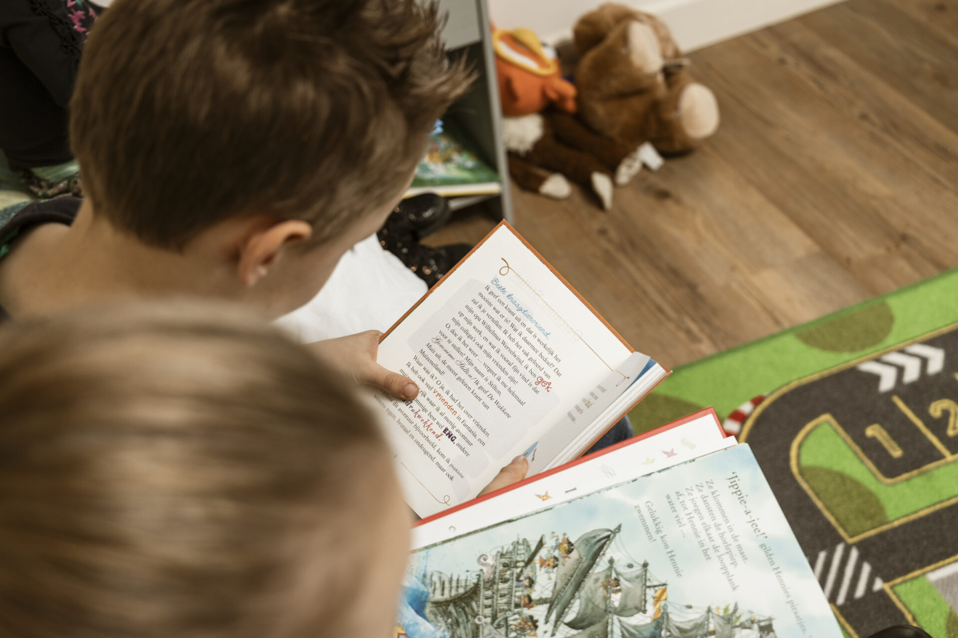 Twee kinderen zitten samen op de grond en lezen aandachtig in hun eigen kleurrijke kinderboeken uit het Boekskes Kleuterpakket.