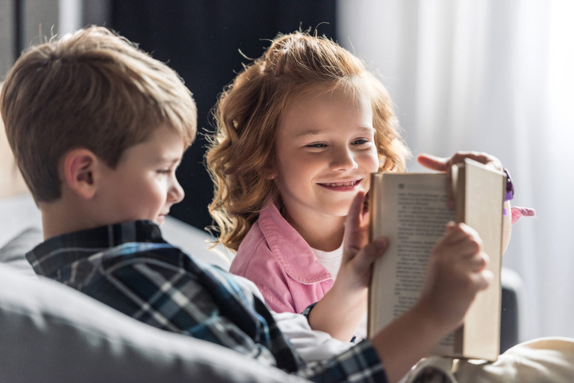 Twee jonge kinderen zitten samen op de bank en lezen vrolijk een boek uit het Boekskes-pakket dat ze samen vasthouden.