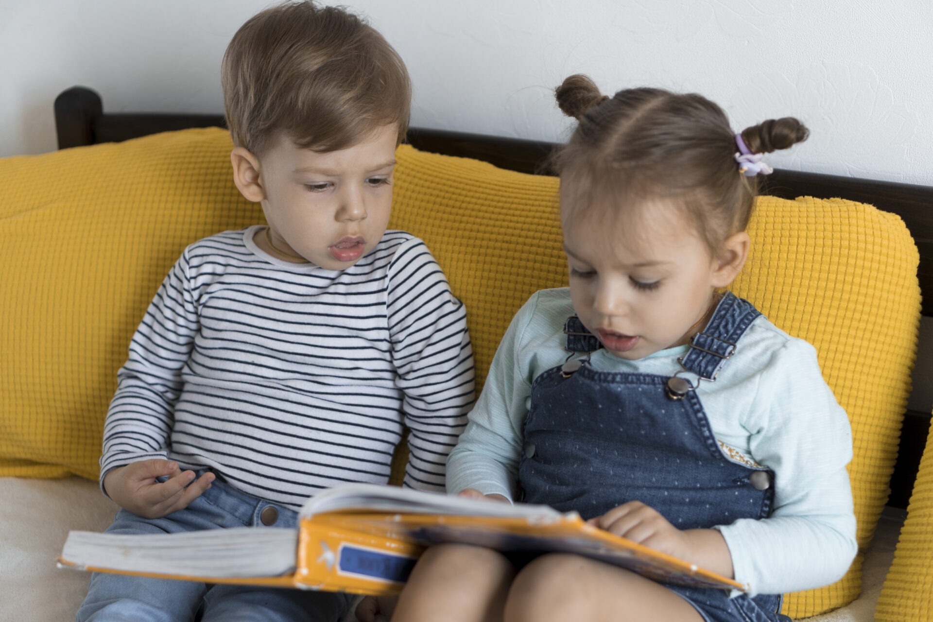 Twee jonge kinderen zitten samen op de bank en lezen aandachtig in een kleurrijk boek uit hun Boekskes-pakket.