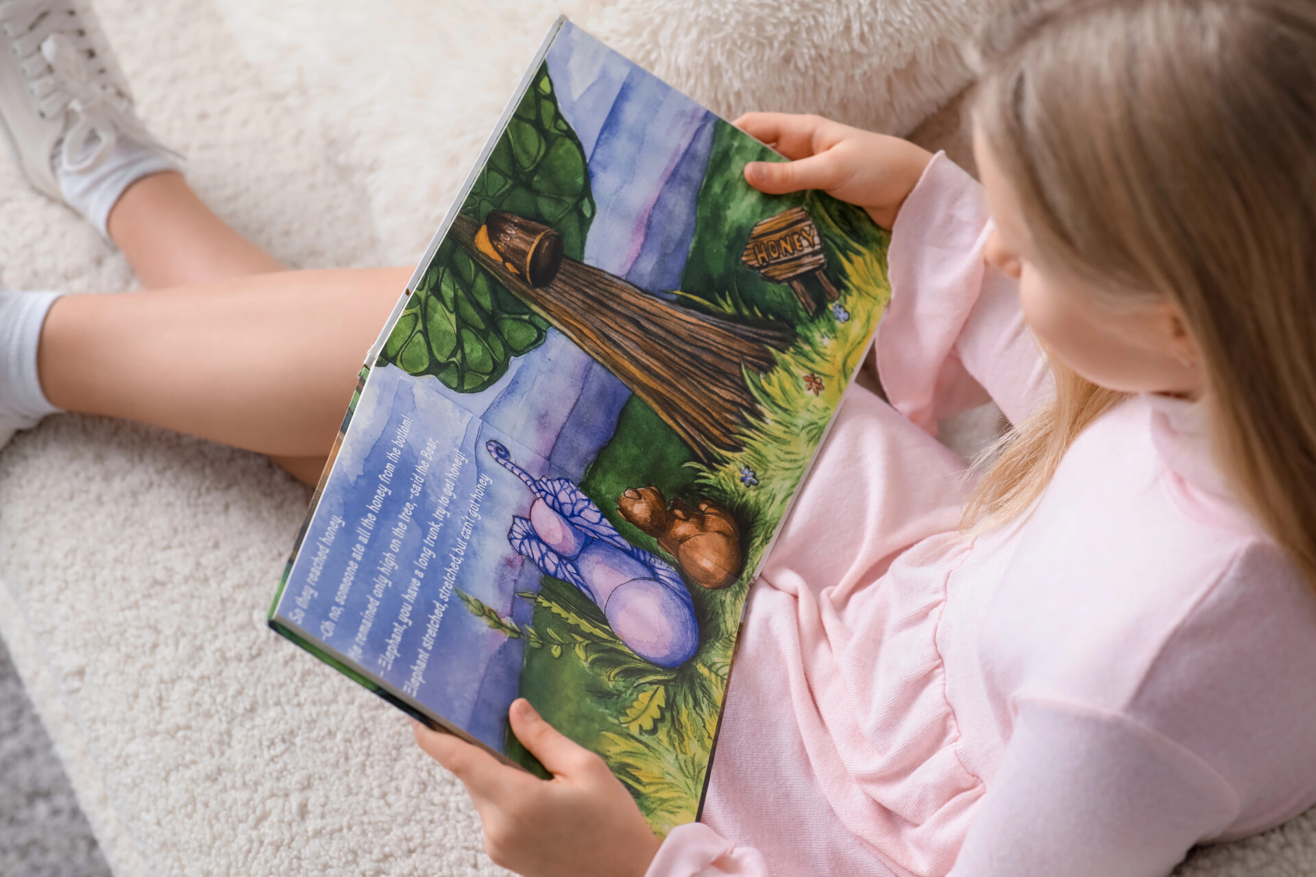 Meisje leest aandachtig een kleurrijk prentenboek uit het Boekskes-pakket van oktober op de bank.