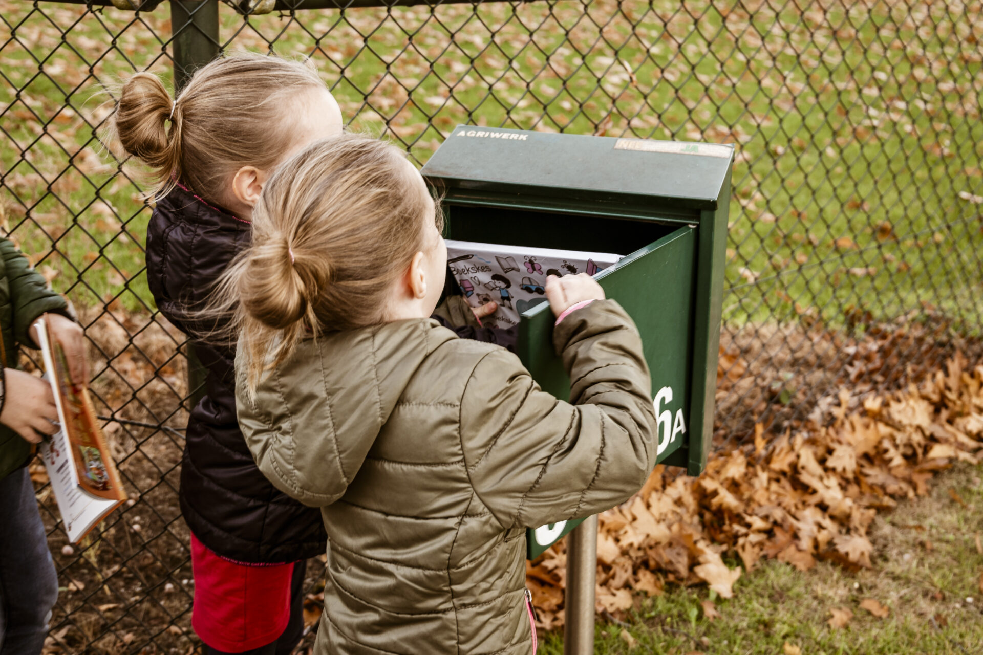 Twee kinderen halen een Boekskes-pakket vol nieuwe kinderboeken uit de brievenbus op een herfstige dag.